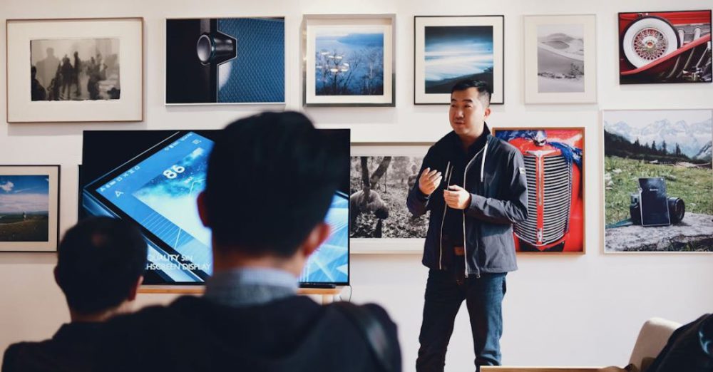 Mentors - Man Beside Flat Screen Television With Photos Background