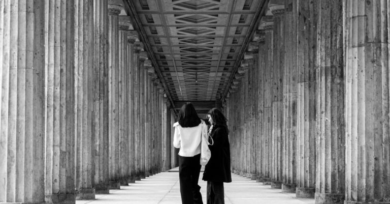 Talks - Two people walking down a long hallway with columns